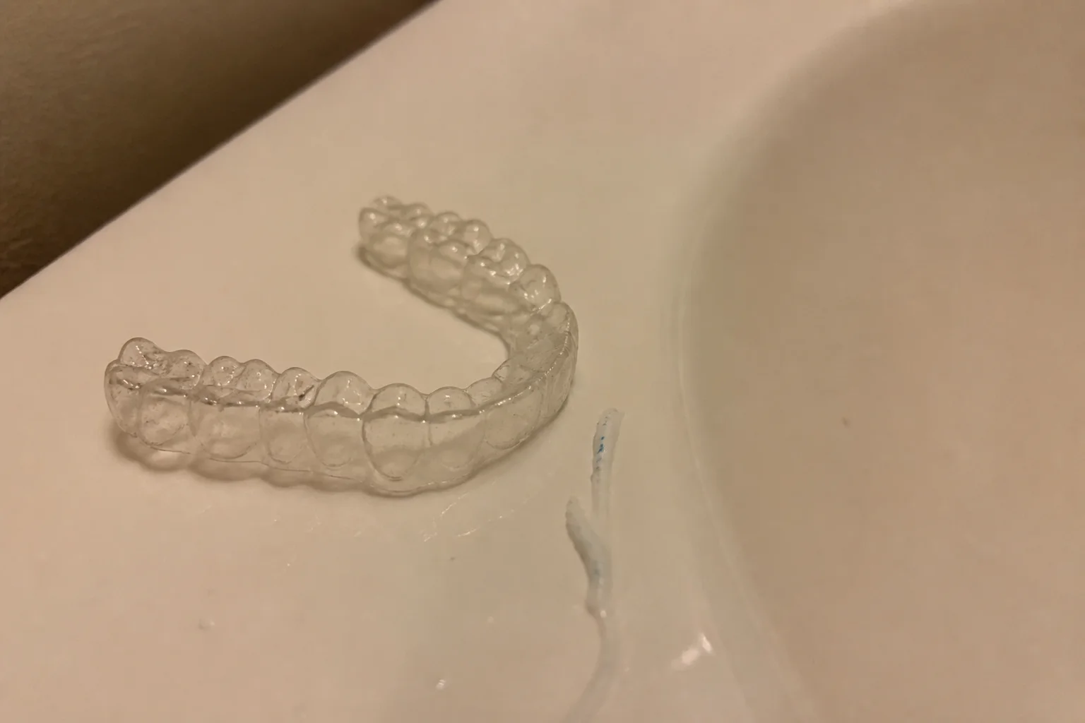 Clear orthodontic retainer resting on a bathroom sink edge