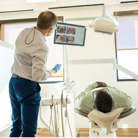 Orthodontist reviewing a 3D scan on a wall screen while a patient relaxes in the treatment chair