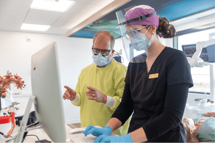 Orthodontist and clinical assistant reviewing a patient’s records together on a computer